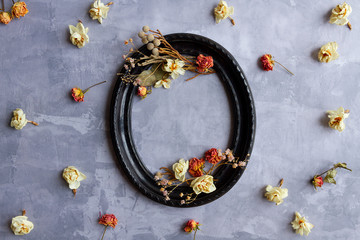 Composition of dried flowers, sprigs, leaves laid out inside black vintage oval frame and scattered around on concrete cement background. Greeting card template. Happy mothers, women day concept.