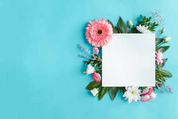 Blank square sheet of paper on blue background. Composition of pink and white flowers are lined with frame around. Greeting card template. Happy mothers, women day, spring, easter concept.