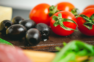 Red cherry tomatoes and black olives on wooden board