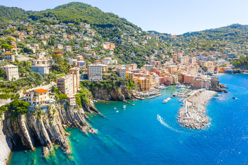 Naklejka premium Marina and breakwater where lighthouse is located. Boat sailing to the harbor in ligurian sea, Camogli near Portofino, Italy. Aerial view on traditional Italian colorful houses