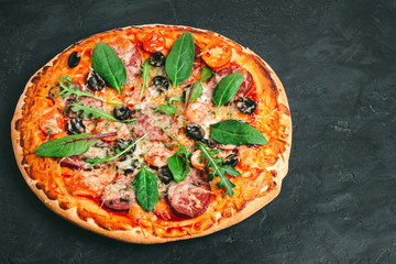 Homemade baked pizza margarita with salami, mozzarella cheese, olives and green leaves