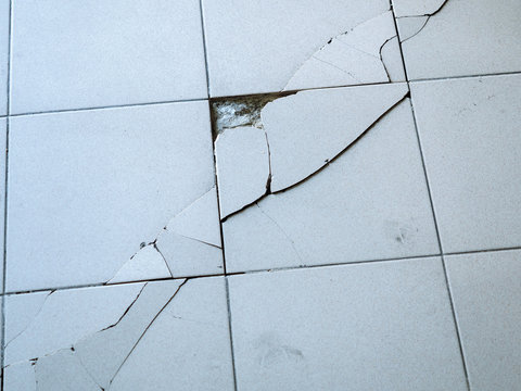 Close-up photo of light gray tile with large diagonal cracks and chips.