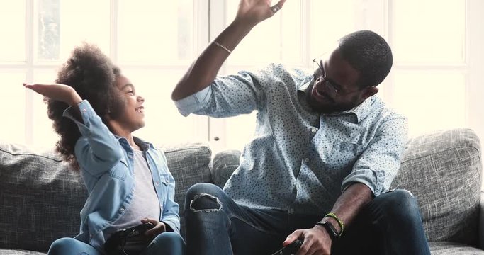 Happy african dad and child daughter playing winning video game