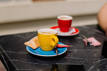 Two bright, multi-colored cups with coffee stand on a table on a sunny day.