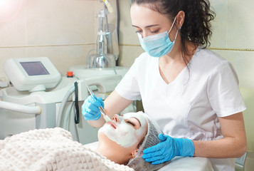 Cosmetologist doing cosmetic face mask treatment for the young woman.