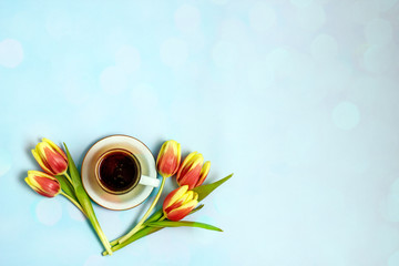 Cup of coffee and tulip on a blue background. A bouquet of five red tulips next to coffee. Coffee and flowers background. The concept of good morning, mother's day, women's day, birthday. Flat lay
