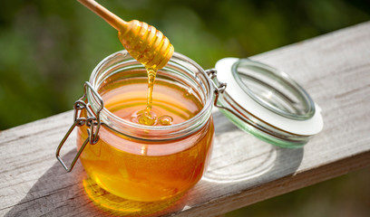 Honey in glass jar on a wooden floor.