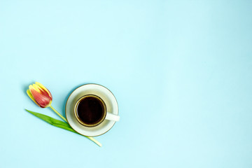 Cup of coffee and tulip on a blue background. A bouquet of five red tulips next to coffee. Coffee and flowers background. The concept of good morning, mother's day, women's day, birthday. Flat lay