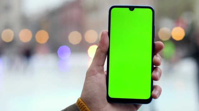 Green screen smartphone on ice rink with city lights on blurred background. Chroma key mockup display for free content. Online connection. Stream trend. Winter holidays abroad. Happy feelings.