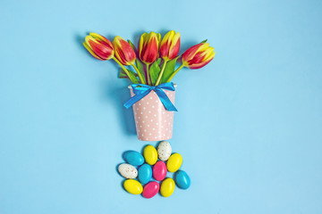 Happy easter day. Easter tulips on a blue background.Yellow tulips next to a small decorative easter multi-colored candy egg on a blue background. Easter concept, top view, flat lay, 