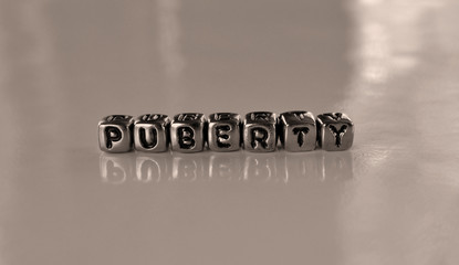 Puberty -  word from metal blocks - concept sepia tone photo on shine background