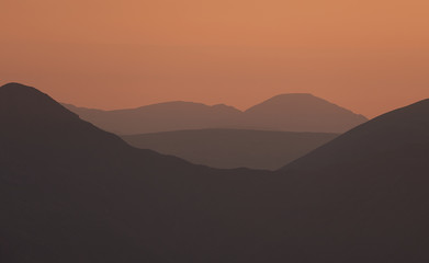 The warm late evening glow of sunset over the mountains of the Lake District with the sun just just after the sun dipped below the ridgeline.