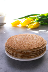 Several pancakes without filling on a white plate on a light gray background. Foreground. The Celebration Of Mardi Gras. Vertical orientation. Flowers in the background. The concept of spring