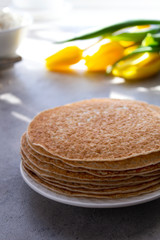 Several pancakes without filling on a white plate on a light gray background. The Celebration Of Mardi Gras. Vertical orientation. Flowers in the background. The concept of spring and holiday