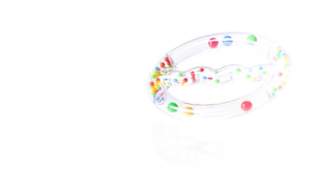 Transparent baby rattle toy spinning on white background in 8x slow motion