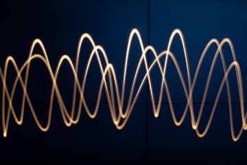 Segni luminosi a forma di onda sinusoidale ottenuti muovendo una torcia elettrica nel buio - obrazy, fototapety, plakaty