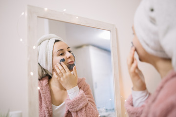 Young girl applying mask on her face in front of a mirror