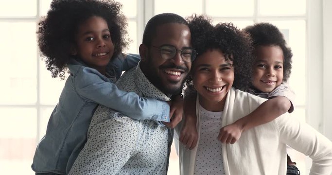 Happy african parents piggyback children look at camera, family portrait