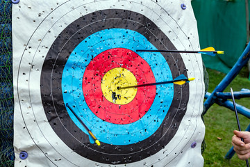 Standard colorful target for archery with arrows. Hand of a man with one arrow after hitting the...