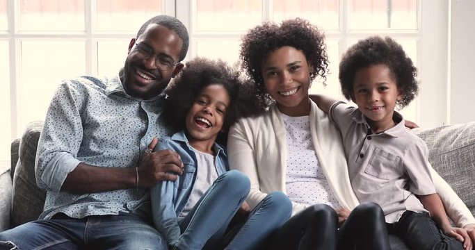 African parents posing for portrait sit with children on sofa