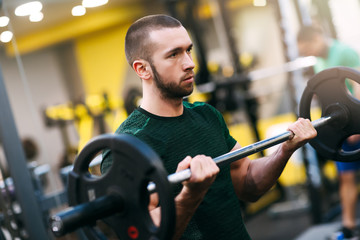 Young fitness man doing barbell curl in gym
