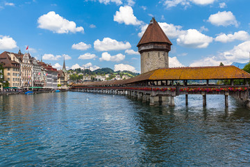 Beautiful view of Chapel Bridge (Kapellbruecke) and Water Tower (Wasserturm) with Lucerne old town in background and Reuss river flowing to lake, on sunny summer day with blue sky cloud, Switzerland