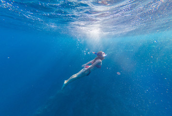 Fototapeta na wymiar Girl with a mask and a snorkel dives into the sea with corals and fish