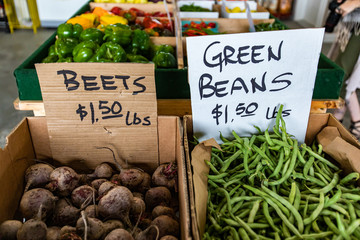 Close up of two cardboard containers with veggies at the food market. Hand written price signs on cardboard sheets. Beets and green beans on sale.