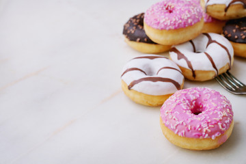 Glazed, chocolate frosted and sprinkled donuts on forks isolated on marble background. Selective focus. Forks Madness set