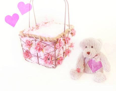 A newborn prop of a basket and a teddy bear with pink roses.