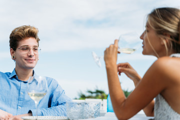 Young man with piercings and glasses looking at a blonde girl drinking water from a glass on a terrace