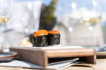 Two pieces of sushi food with fish eggs served on a wood small board in a table with glasses of...