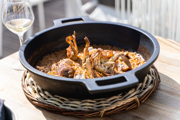 Rice with seafood served in a iron pot in a wood table with a glass of wine