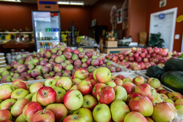 Close up of neatly arranged container filled with crisp yellow and red apples. Many other apples in the background, Shop interior.