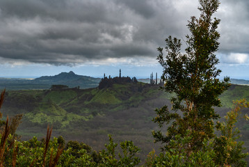 Kauai, Hawaii, USA. - January 11, 2012: Dark rainy cloudscape with blue at the horizon over green, wild, hilly hinterland. Green tree foliage up front. 