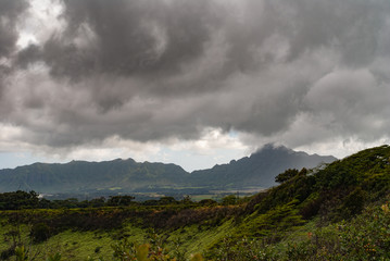 Kauai, Hawaii, USA. - January 11, 2012: Dark rainy cloudscape with light blue at the horizon over green, wild, hilly hinterland. Mountains with dark shadows in back.