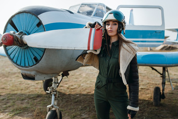 girl stands with her hand on the blade of an airplane propeller in a pilot's helmet