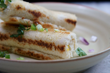 A stack of  toasted bread filled with a mixture of cheese, onion, peppers and cilantro on a plate.