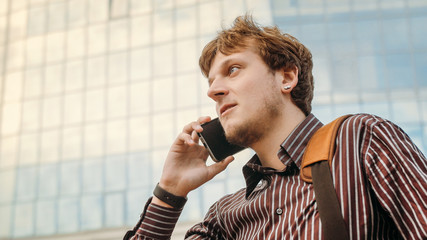 Young man talking on smartphone on the street near business center. Businessman makes an appointment and conduct preliminary negotiations. Man using smart watch app. Business and digital technology.