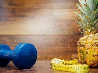 Diet weight loss fitness health care concept with measure tape, pineapple, fitness dumbbell, fitness tracker bracelet. Pineapple, metric ribbon on wood background. Diet heathy lifestyle.