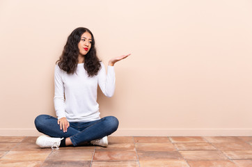 Young woman sitting on the floor holding copyspace with doubts