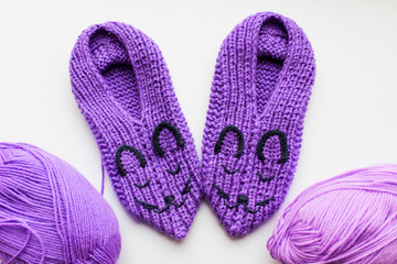 Handmade knitted pink slippers with muzzles. On a white background, surrounded by balls of yarn