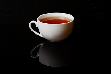 Cup with black tea on a black background. White cup of hot aromatic black tea. Energy drink for breakfast.