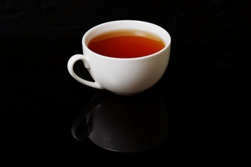 Cup with black tea on a black background. White cup of hot aromatic black tea. Energy drink for breakfast.