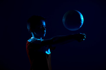 Kid playing volleyball isolated on black background in mixed light. Blue filter