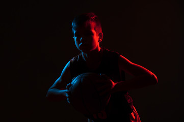 Kid playing basketball isolated on black background in mixed light