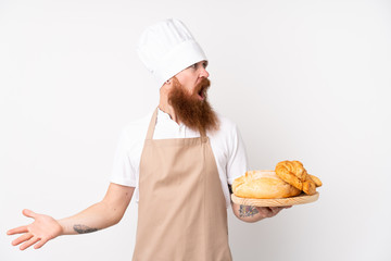 Redhead man in chef uniform. Male baker holding a table with several breads with surprise facial expression