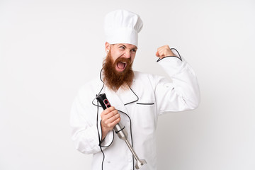 Redhead man using hand blender over isolated white background celebrating a victory