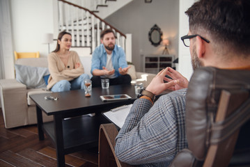 Close up of male psychologist sits at chair and listens depressed young couple at stylish cozy...