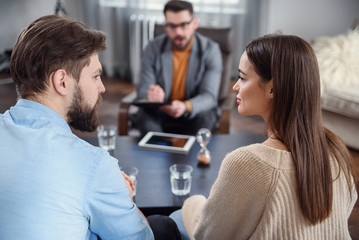 Depressed young couple of man and woman speaking with psychologist on therapy session in modern office. Bad relationships without future.